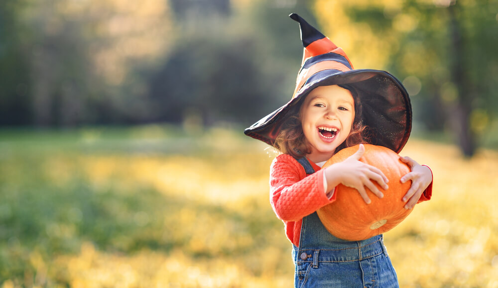 Happy Child Girl With Pumpkin Outdoors in Halloween