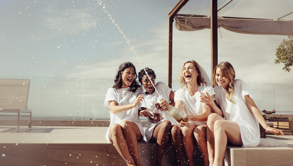 Cheerful Bride and Bridesmaids Celebrating Hen Party With Champagne While Sitting on Rooftop