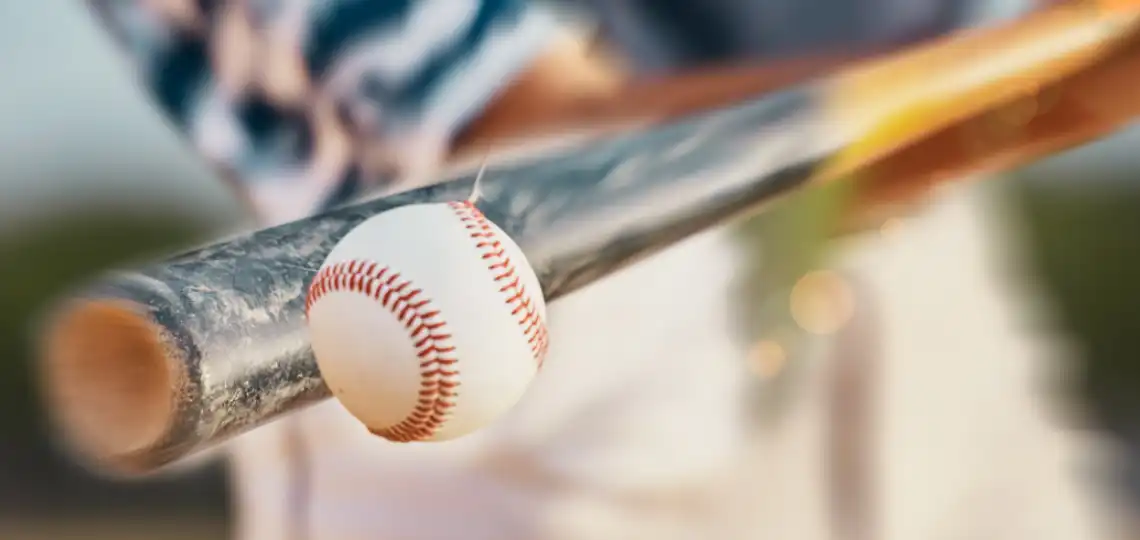 Close-up of a baseball resting on a wooden bat with a blurred background, ready for a hit.