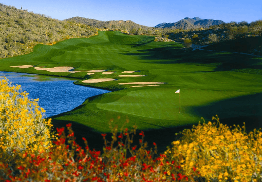Lush golf course green with a flag, surrounded by sand bunkers and a water hazard to the left, framed by autumn flowers.